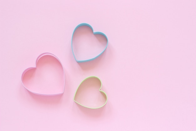 Las galletas de los cortadores de Colorfed en corazón forman en fondo rosa en colores pastel. Tarjeta de San Valentín concepto.