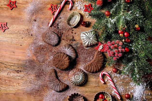 Galletas de corteza corta de Navidad tradicionales caseras medias lunas de chocolate con azúcar glas de cacao en placa de cerámica con moldes de galletas, abeto, decoraciones de estrellas de Navidad rojas sobre fondo de madera
