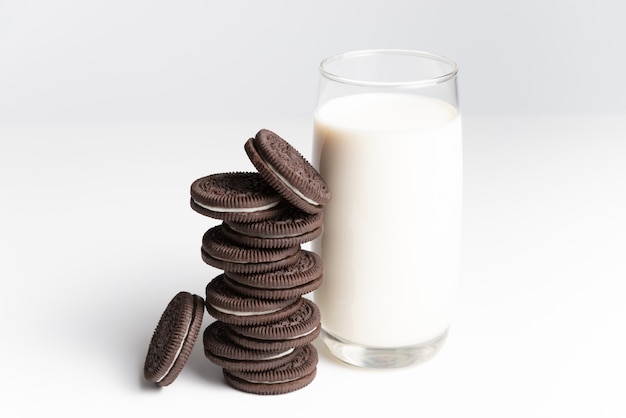 Foto galletas y crema de sabor a chocolate en la pila con vaso de leche fresca en backgrou blanco