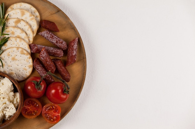 Galletas crujientes, tomates cherry, uvas y tazón de queso sobre tabla de madera