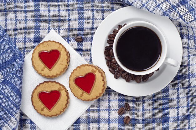 Galletas dulces con azufaifo en forma de corazones y una taza de café negro sobre un mantel azul, vista superior