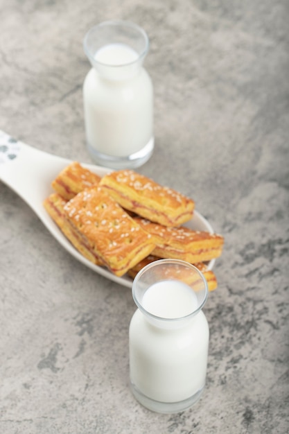 Galletas enteras con semillas de sésamo y jarras de leche de vidrio colocadas sobre una mesa de piedra.