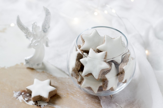 Galletas Estrella de canela en un jarrón de vidrio decorado con una figura de un ángel y una guirnalda.