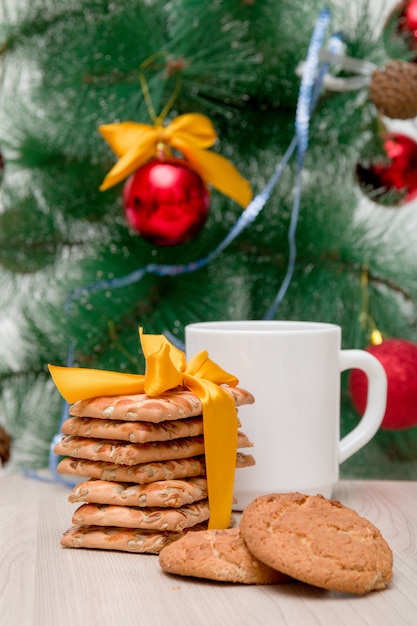 Galletas festivas y una taza blanca sobre un fondo de un árbol de Navidad decorado, fondo de Navidad, año nuevo 2020