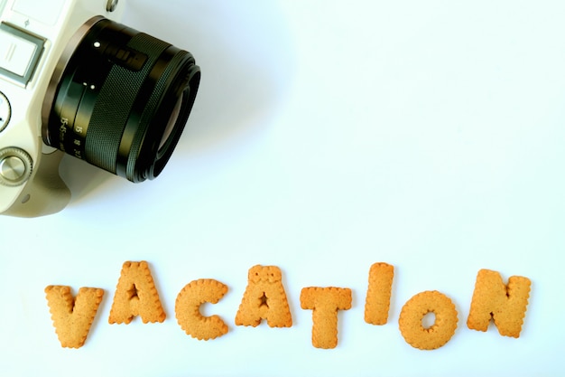 Galletas en forma de alfabeto que deletrea la palabra VACACIONES con una cámara en una mesa azul claro