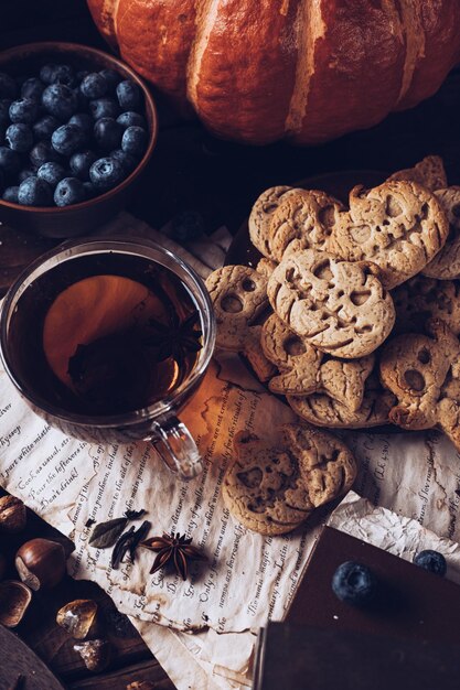 Las galletas en forma de calabazas y fantasmas están en un plato sobre la mesa Junto a una tetera y tazas, un bodegón de otoño