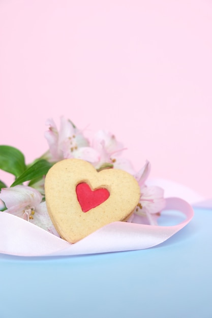 Galletas en forma de corazón con una cinta rosa sobre una rosa