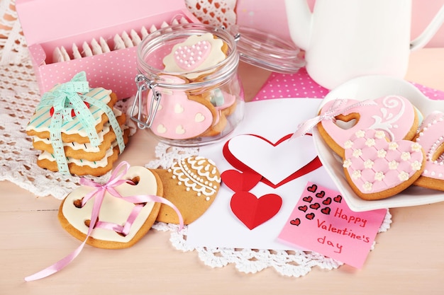 Galletas en forma de corazón para el día de san valentín en plato, bolsitas de té y tarjeta sobre fondo de madera de color