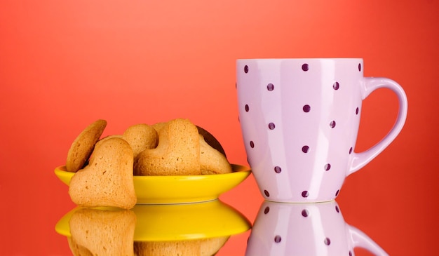 Galletas en forma de corazón en placa amarilla y taza sobre fondo rojo.