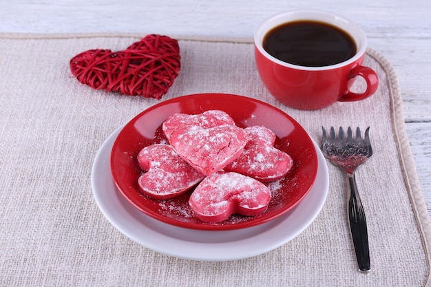 Galletas en forma de corazón en un plato con una taza de café en una servilleta y fondo de tablones de madera de color