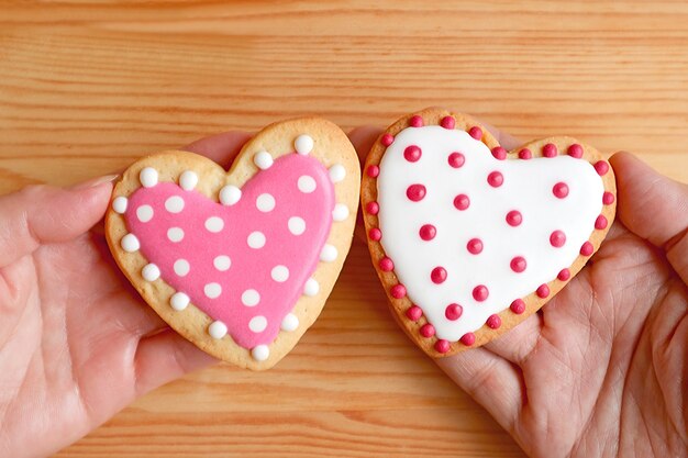 Galletas en forma de corazón punteado rosa y blanco en manos de la pareja juntas