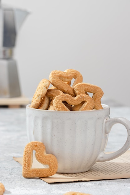 Galletas en forma de corazón en una taza blanca Fondo claro con una cafetera