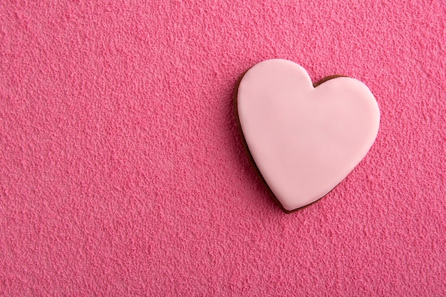 Galletas en forma de corazones con glaseado de azúcar sobre fondo rosa.