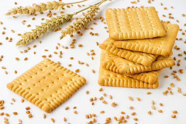 Galletas de forma cuadrada sobre una mesa blanca. Espigas y granos de trigo