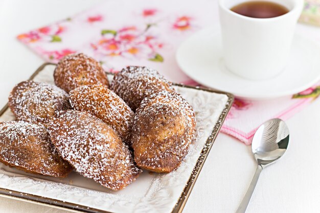 Galletas francesas Madeleine y té en taza blanca.