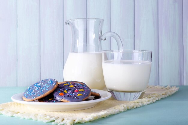 Galletas glaseadas con vaso y jarra de leche sobre fondo de madera de color