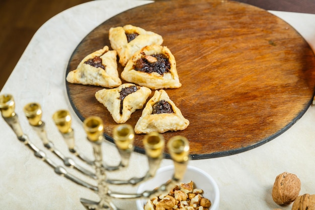 Galletas gomentashi para las vacaciones de Purim en una mesa sobre una tabla de madera junto a la menorá