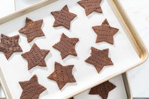 Galletas graham de chocolate en forma de estrella sin hornear en la bandeja para hornear forrada con papel pergamino