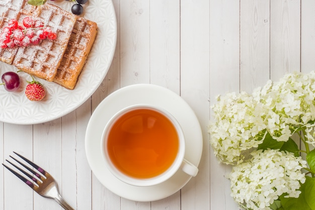 Galletas hechas en casa con las bayas del verano en una placa. Una taza de té en una mesa de luz. Enfoque selectivo