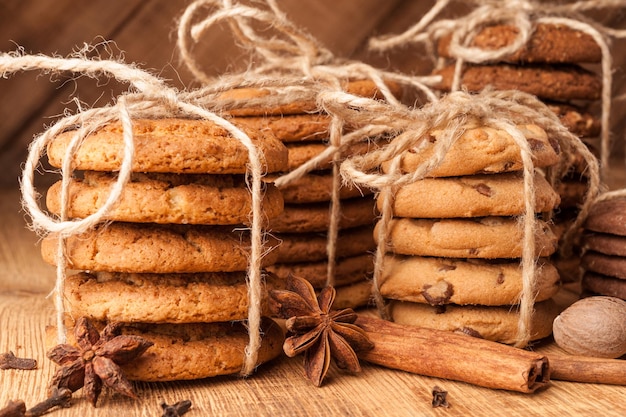 Galletas integrales con cable caseras con avena, lino y semillas de sésamo y galletas tradicionales con chispas de chocolate en la mesa de madera rústica oscura y especias.