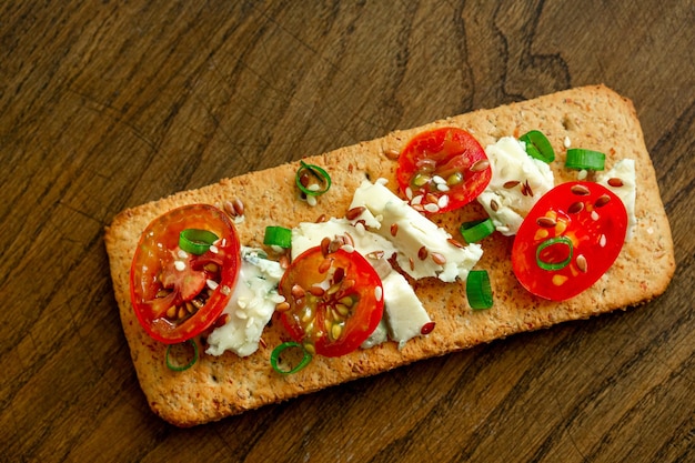 Galletas integrales pan crujiente fino con queso tomates cebolla verde y semillas de lino sobre fondo de madera natural