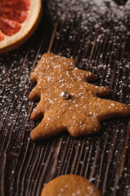 Galletas de jengibre en abeto de Navidad con azúcar en polvo sobre mesa de madera, pomelo seco cítrico, ángulo de visión, enfoque selectivo