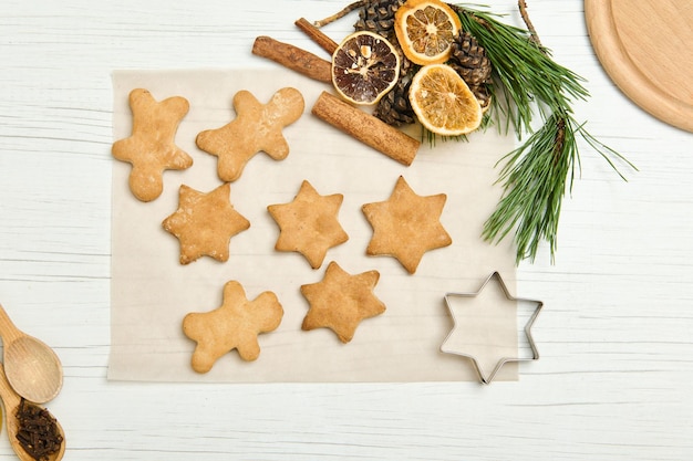 Galletas de jengibre en forma de estrella para Navidad, sobre papel pergamino con piñas y ramas, rodajas secas de naranja y palitos de canela