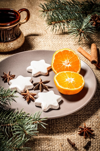 Galletas de jengibre en forma de estrella en plato con canela, anís estrellado y ramas de abeto natural con conos, taza de café en cilicio. Efecto tonificante de color.