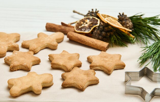 Foto galletas de jengibre en forma de estrellas para navidad, sobre una superficie de madera con conos y ramas de pino, rodajas secas de naranja y palitos de canela