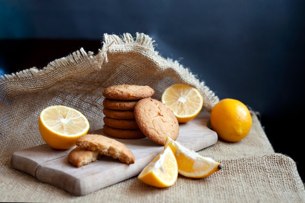 Las galletas de jengibre de limón se encuentran en una tabla de madera sobre una mesa rústica, bodegón de galletas frescas con cítricos, espacio de copia