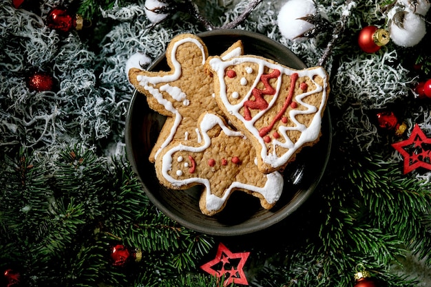 Galletas de jengibre navideñas tradicionales caseras con glaseado adornado. Hombre de pan de jengibre, ángel, campana en plato de cerámica con adornos navideños y abeto. Endecha plana