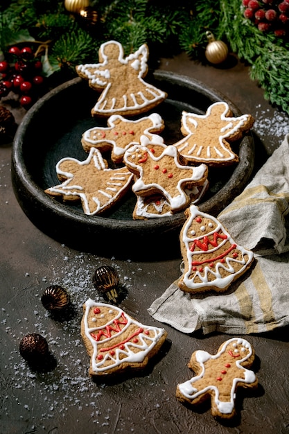 Galletas de jengibre navideñas tradicionales caseras con glaseado adornado. Hombre de pan de jengibre, ángel, campana en plato de cerámica con adornos navideños.