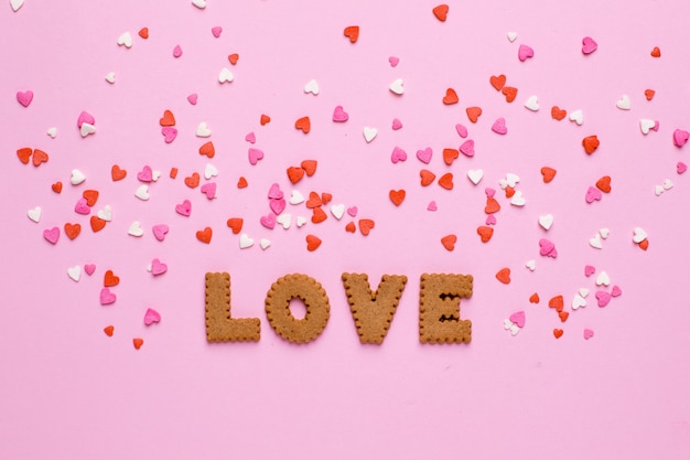 Galletas de letras Amor con corazones rosas y rojos sobre rosa