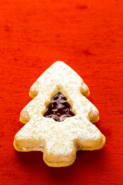 Galletas Linzer en forma de árbol de Navidad sobre fondo rojo.