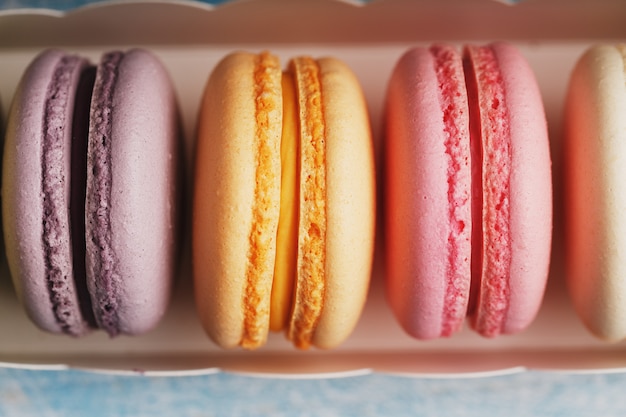 Galletas de macarrones de diferentes colores en una caja sobre un fondo de madera azul, viejo de color azul.