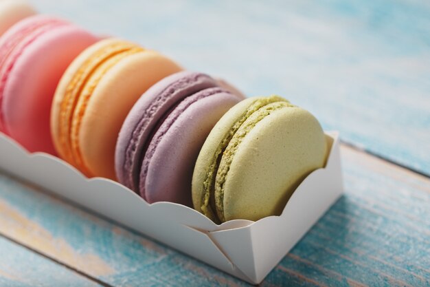 Galletas de macarrones de diferentes colores en una caja sobre un fondo de madera azul, viejo de color azul.