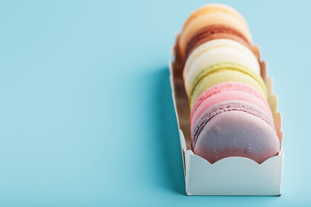 Galletas de macarrones de diferentes colores en un cuadro blanco sobre un fondo azul.