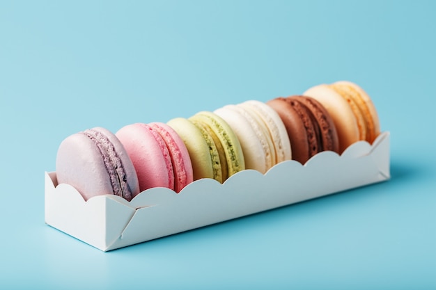 Galletas de macarrones de diferentes colores en un cuadro blanco sobre un fondo azul.