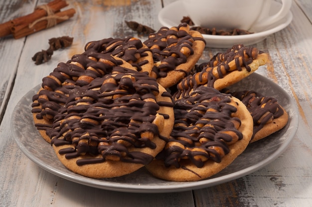 Galletas con maní y chocolate sobre una mesa de madera clara con una ramita de canela