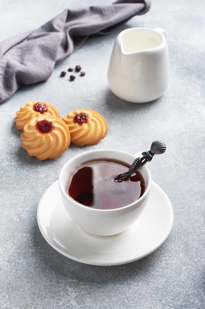 Galletas de mantequilla Kurabye con mermelada de frutos rojos en un plato y una taza de té. Delicioso postre, fondo de hormigón gris con espacio de copia.