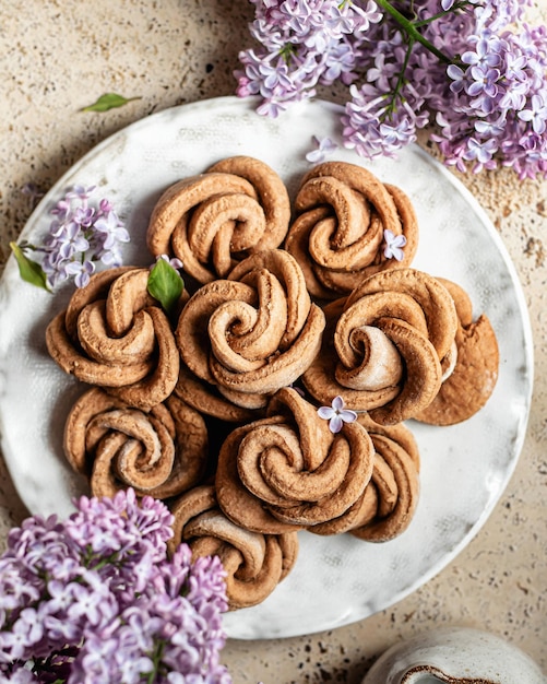 Galletas de mantequilla de requesón en forma de rosa en un plato Acogedor bodegón con flores de color lila Vista superior