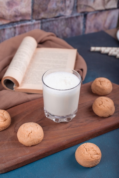 Galletas de mantequilla y un vaso de leche sobre una tabla para cortar madera. Vista superior