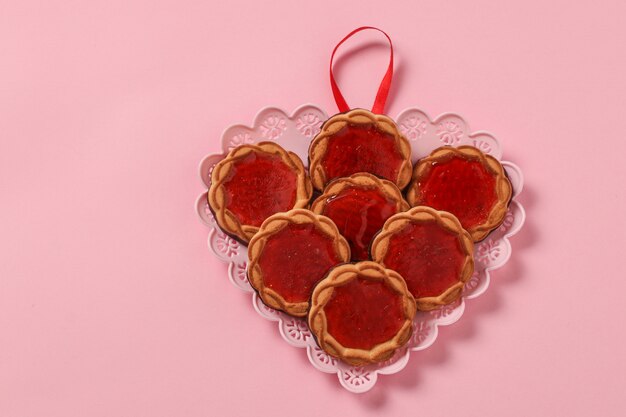 Galletas con mermelada de bayas en un plato en forma de corazón para San Valentín en rosa