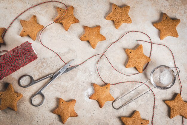 Galletas de Navidad caseras de pan de jengibre con azúcar en polvo, cuerda de decoración verde-roja en piedra clara, vista superior, copyspace