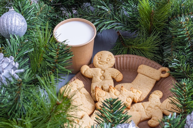 Foto galletas de navidad, galletas de jengibre y un vaso de leche en un vaso artesanal para santa con ramas de abeto y adornos navideños. fondo de navidad.