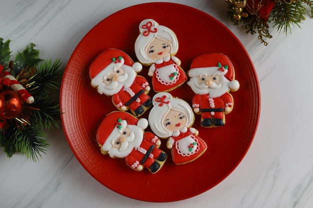 Galletas navideñas con forma de Papá Noel, muñeco de nieve y jengibre servidas en el plato rojo.