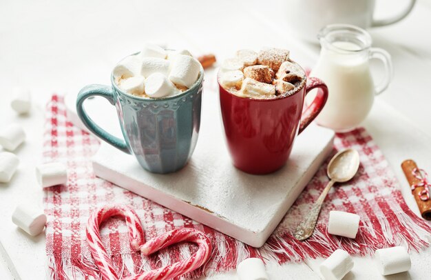 Galletas navideñas, leche, cacao, malvaviscos, dulces en un plato blanco junto a la ventana