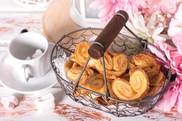 Galletas de orejas dulces en una canasta de metal Flores y dulces sobre un fondo blanco