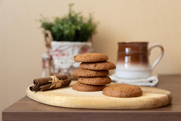 Galletas de pasas de avena en una tabla de madera con palitos de canela y una taza de leche Pastelería casera tradicional en estilo rústico Primer plano de enfoque selectivo