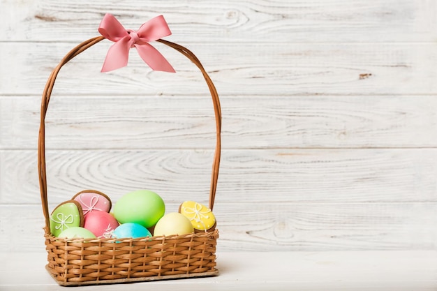 Galletas de Pascua coloridas en cesta con huevos de Pascua de varios colores sobre fondo de color Concepto de vacaciones de huevos de Pascua de color pastel con espacio de copia